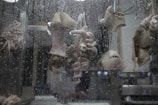 Various cuts of meat, possibly tripe and intestines, are hanging on hooks behind a window covered with water droplets.