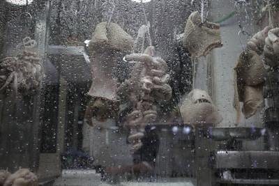 Various cuts of meat, possibly tripe and intestines, are hanging on hooks behind a window covered with water droplets.