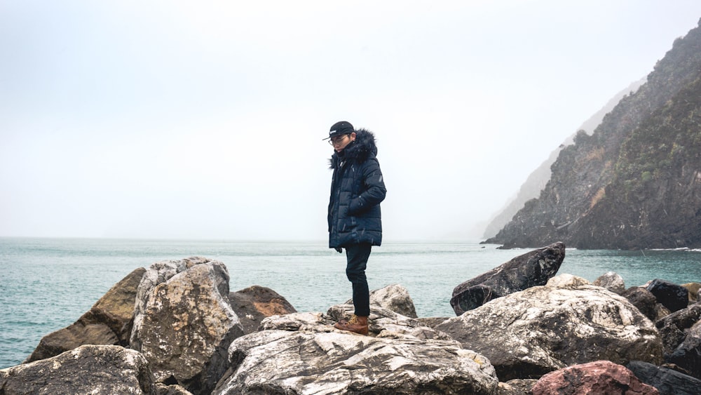 man standing on stone beside body of water