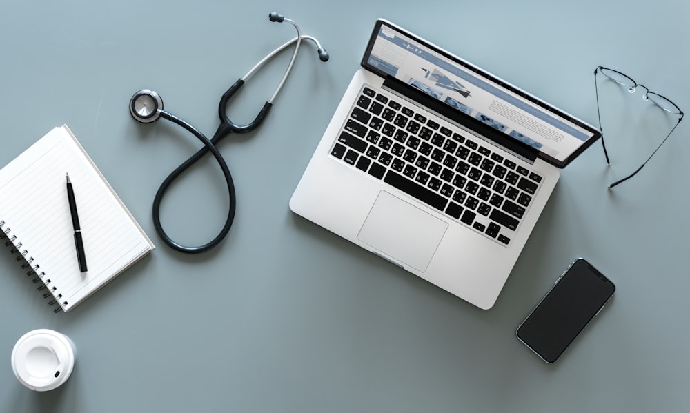 flat lay photography of MacBook Pro, stethoscope, phone, and notebook