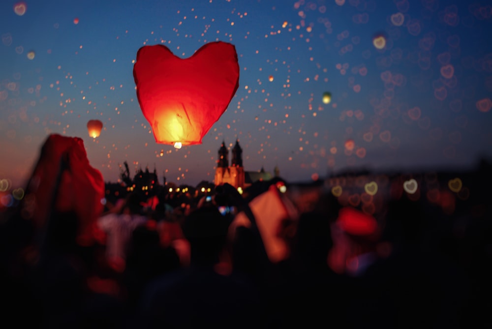 folla di persone che fanno volare lanterne a cuore nel cielo