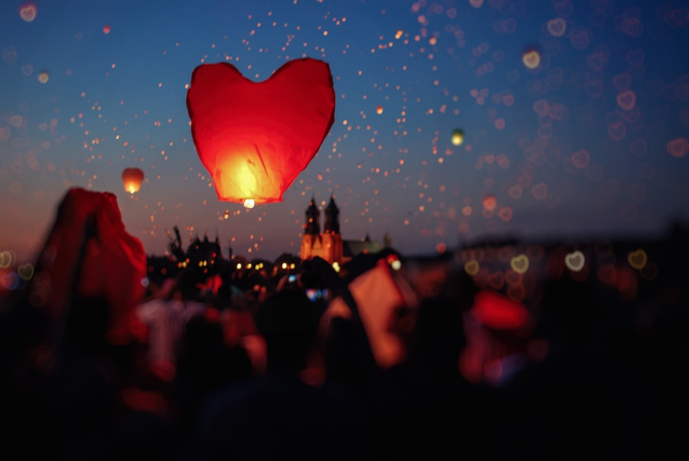 foule de gens volant des lanternes en forme de cœur dans le ciel