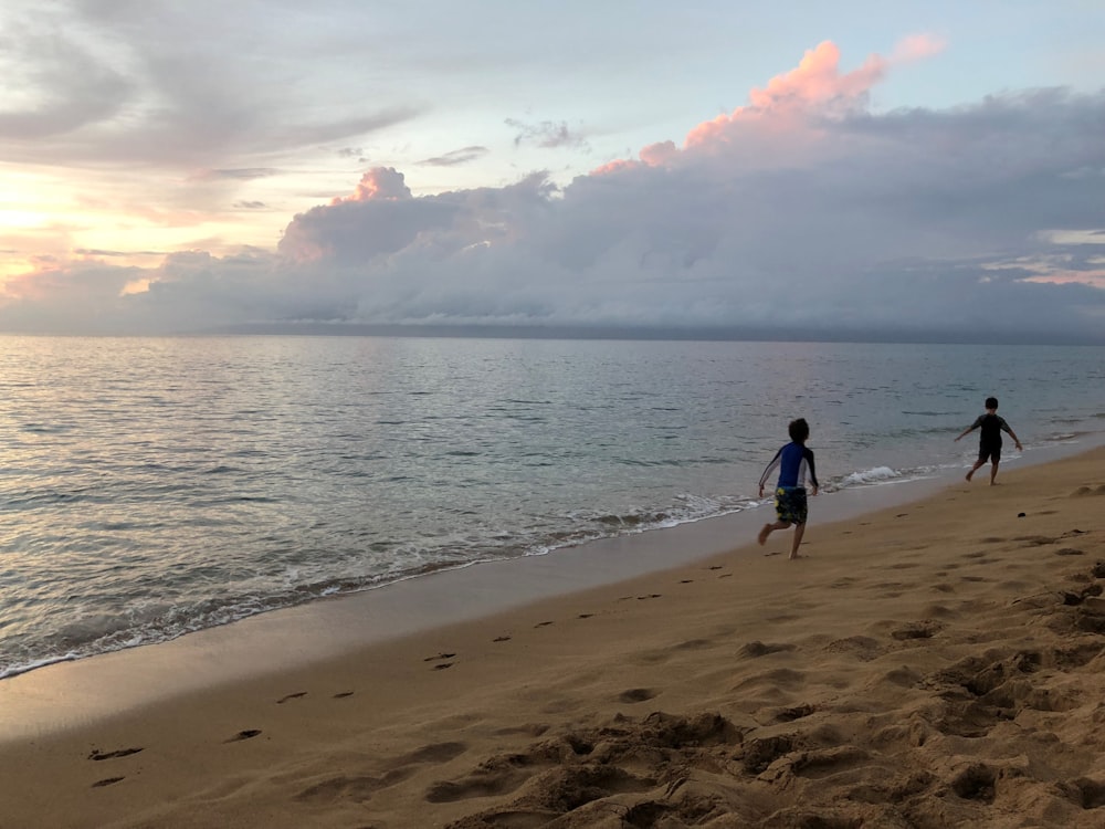 zwei Kinder laufen bei Sonnenuntergang am Strandufer