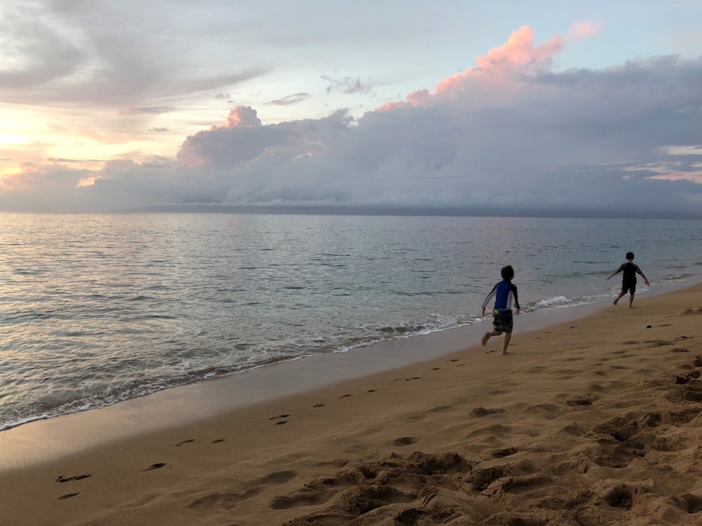 Dos niños corriendo en la orilla de la playa durante la puesta del sol