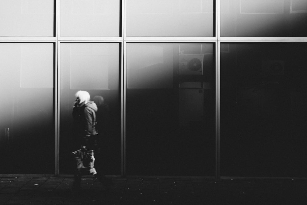 grayscale photography of person walking near glass window building