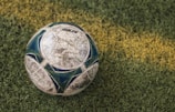 A well-worn soccer ball resting on a grassy field, with a distinct yellow line running across the grass.