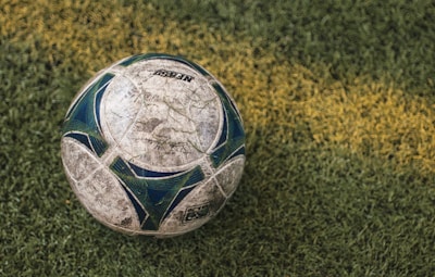 A well-worn soccer ball resting on a grassy field, with a distinct yellow line running across the grass.