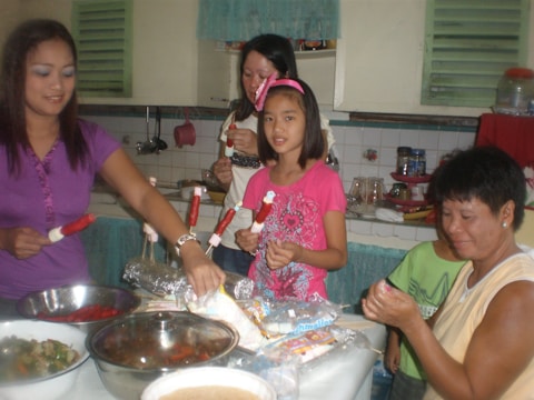 A group of volunteers smiling warmly as they prepare food packages in a bright community kitchen.
