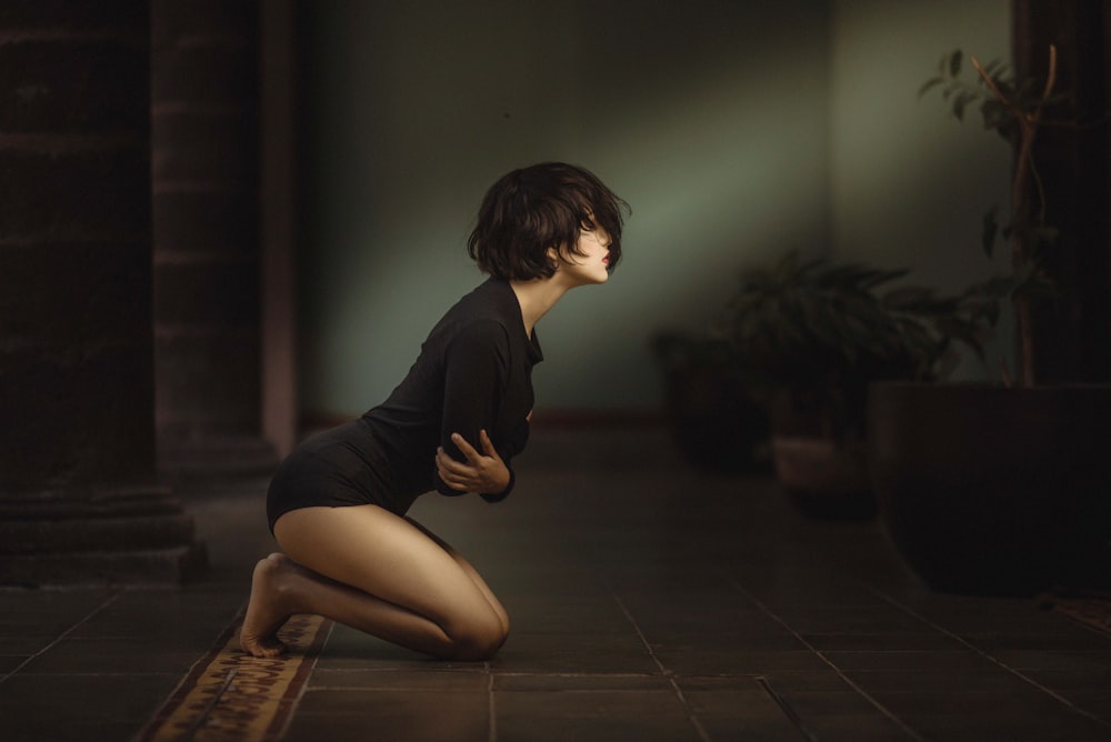 woman kneeling with arms folded over chest inside dim-lit room