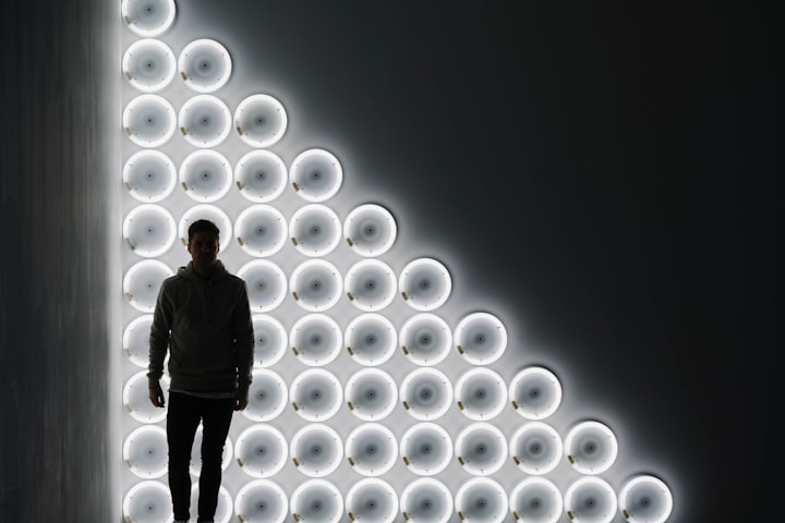 Photo of a person seen in silhouette in front of a series of circular lights, arranged in a large triangle