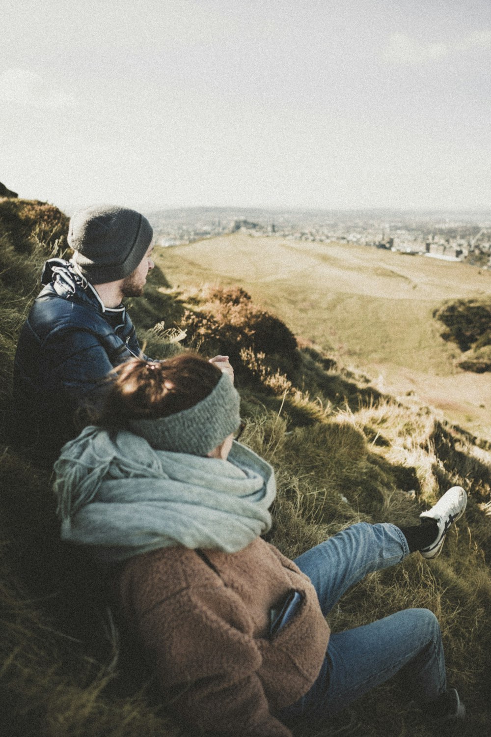 uomo e donna che si siedono sull'erba verde mentre guardano la città durante il giorno