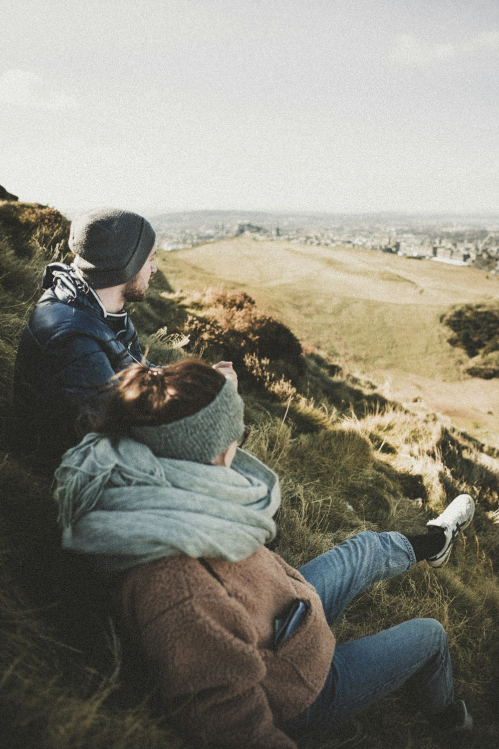 man and woman sitting on green grass while looking at city during daytime