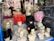 Mannequin heads with various styles of wigs are displayed in a store window. The wigs come in multiple colors, including blonde, black, pink, and bright red. The wigs are styled in elaborate and voluminous fashion, giving a vibrant and eclectic appearance. The reflection of buildings and trees outside can be seen on the window glass.