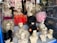 Mannequin heads with various styles of wigs are displayed in a store window. The wigs come in multiple colors, including blonde, black, pink, and bright red. The wigs are styled in elaborate and voluminous fashion, giving a vibrant and eclectic appearance. The reflection of buildings and trees outside can be seen on the window glass.