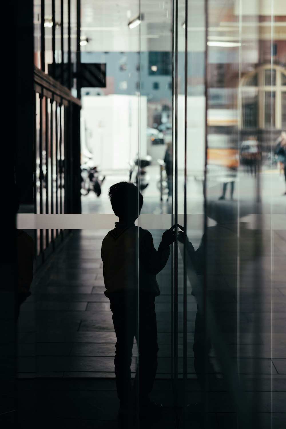 ガラスの壁のそばに立つ男の子のシルエット写真