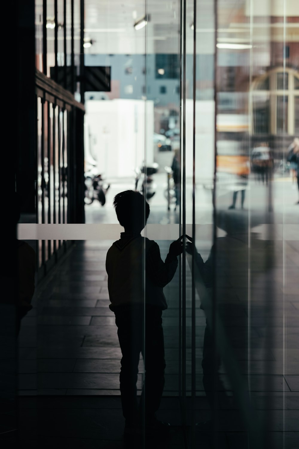 silhouette photo of boy standing near glass wall