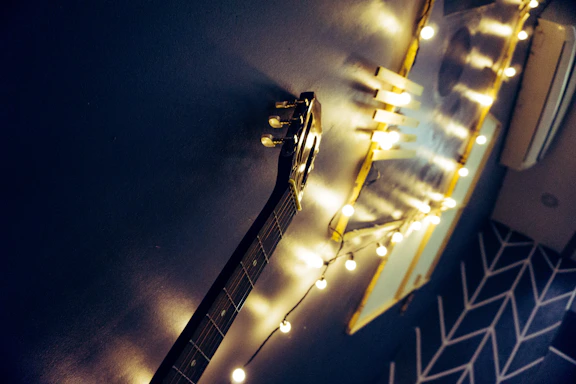 A dimly lit guitar resting against a deep purple wall with warm orange light casting soft shadows.