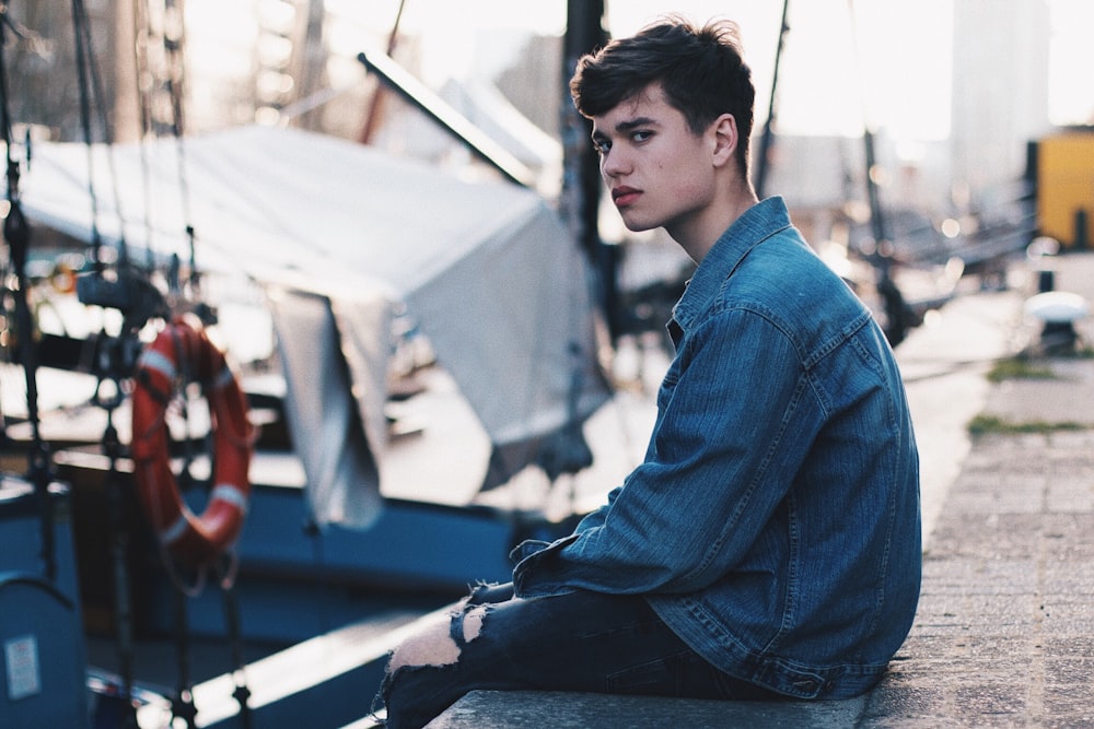 man in blue denim jacket sitting on dock