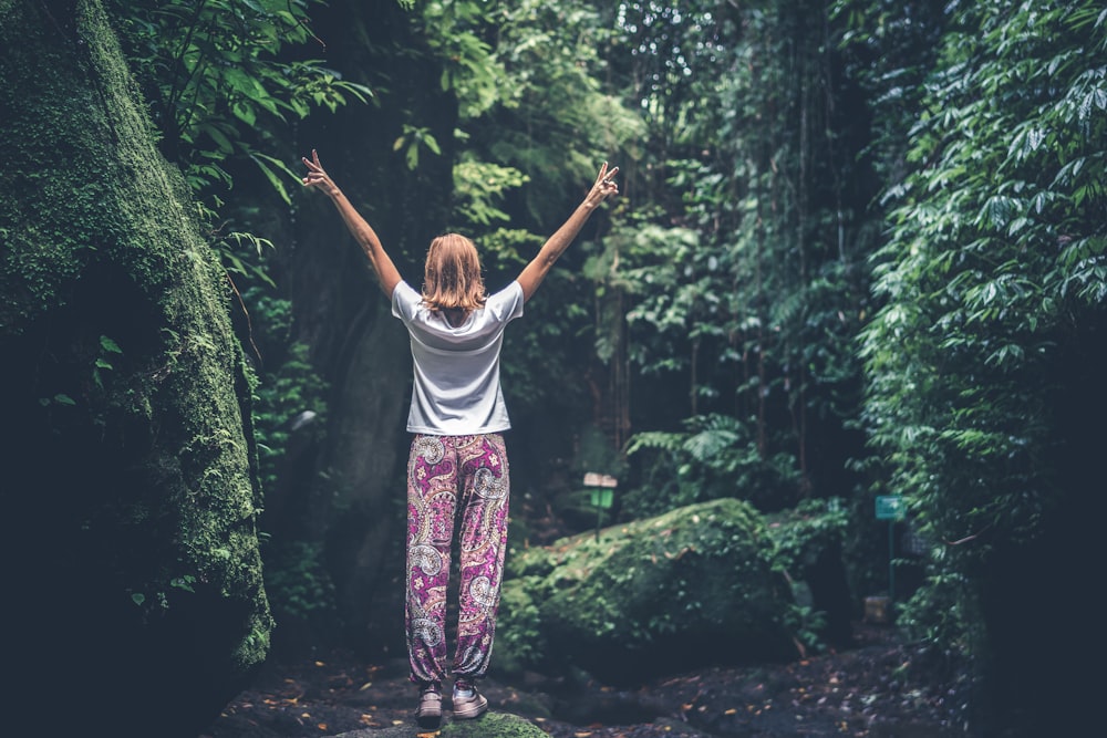 woman standing on rock making peace sign in forest