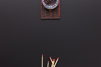 A compass is positioned at the top against a dark background, with several wooden matches arranged at the bottom, their red tips pointing upwards.