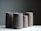 Four tall, cylindrical ceramic pitchers with a minimalist design are arranged on a white surface against a muted gray background. Each pitcher has a matte finish with slight variations in tone, ranging from dark to light grayish-brown.