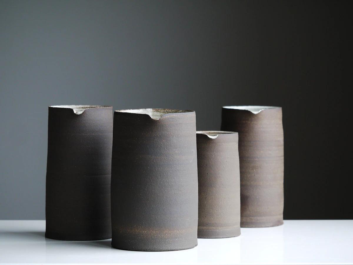 Four dark grey stoneware pitchers lined up on a white surface