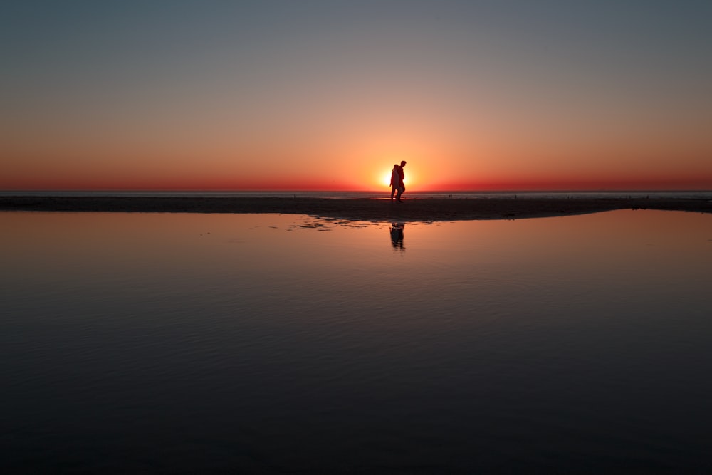 person standing across water during sunset
