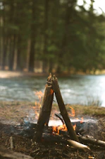 Authentic image of a campfire glowing quietly among trees with hunting gear and rugged tools placed nearby.