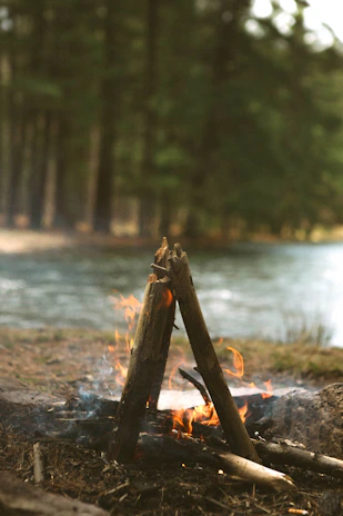 Authentic image of a campfire glowing quietly among trees with hunting gear and rugged tools placed nearby.