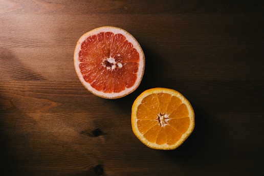 two orange and grapefruit halves on brown wooden surface