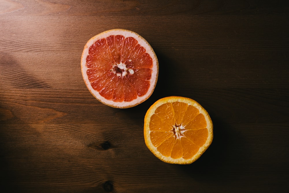 two orange and grapefruit halves on brown wooden surface