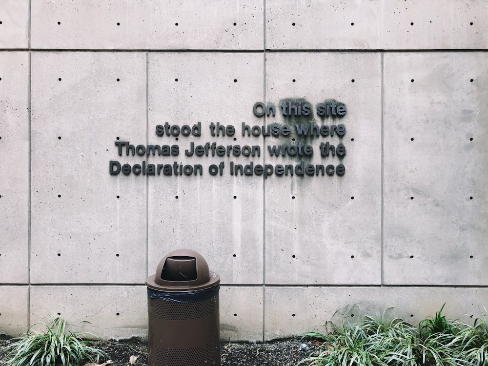 brown trash bin in front of gray wall