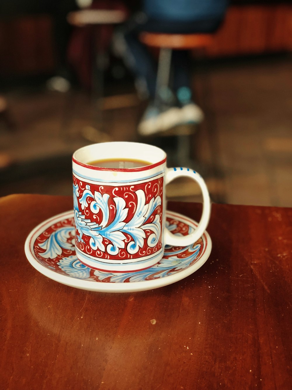 white and red ceramic mug on saucer with brown liquid