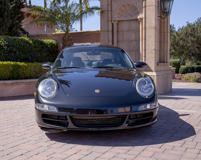 A sleek black Porsche parked in front of a modern luxury villa at sunset.