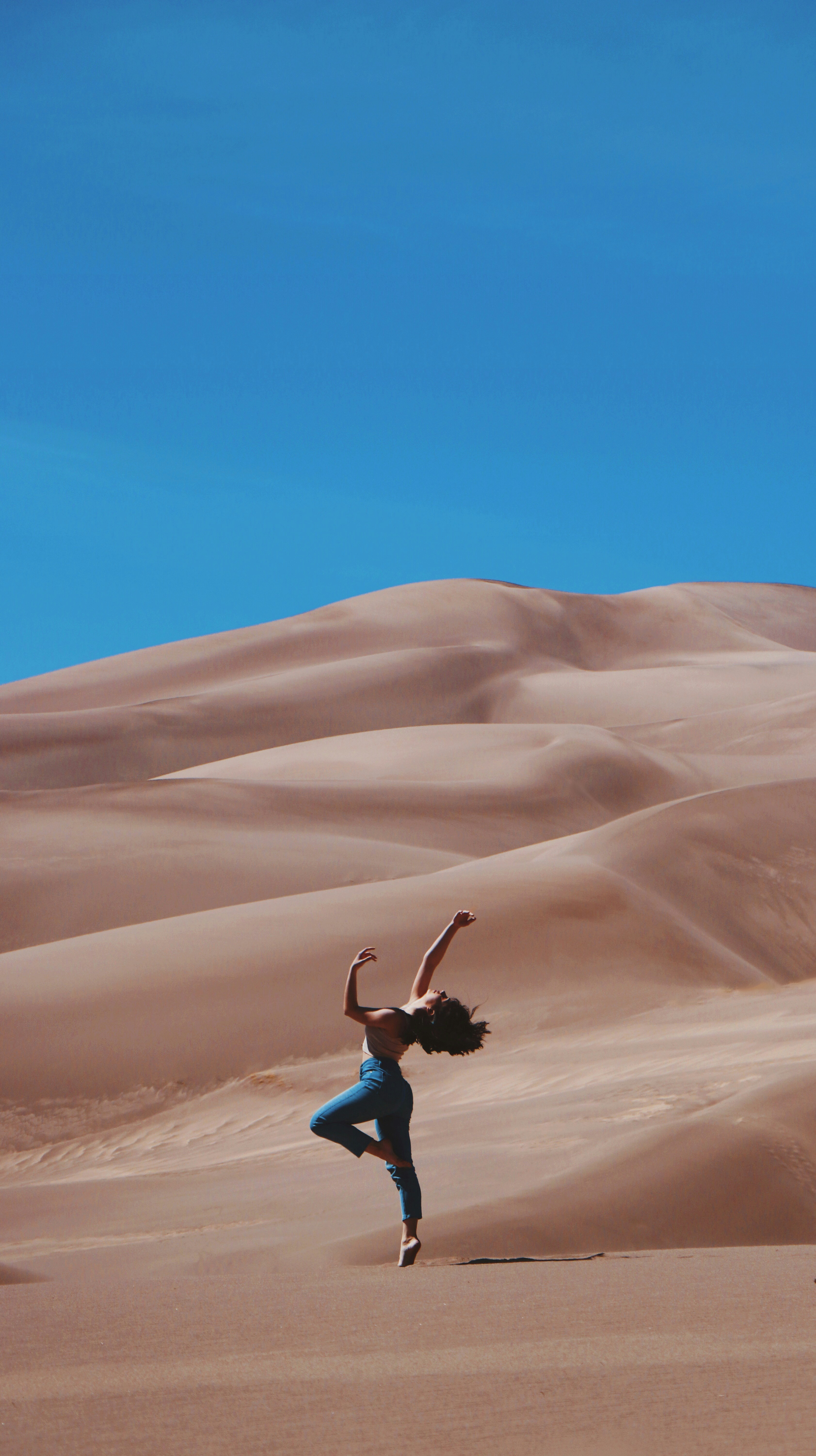 great photo recipe,how to photograph sand dancer; woman standing on right foot and raising hands at the bottom of sand dunes during daytime