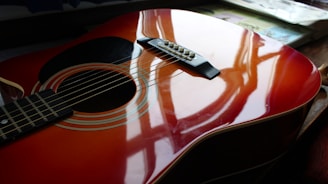 Close-up of a guitar with crimson reflections on a shadowy background.