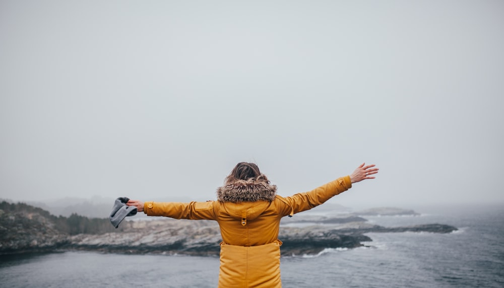 femme écartant les bras tout en regardant l’océan