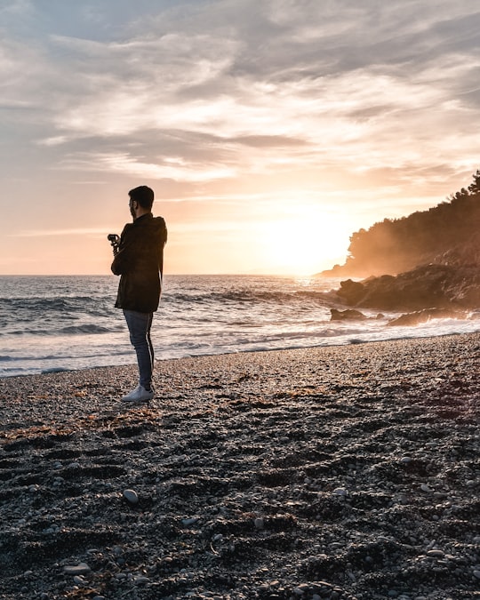 man wearing jacket standing on beach during golden hour in Maratea Italy