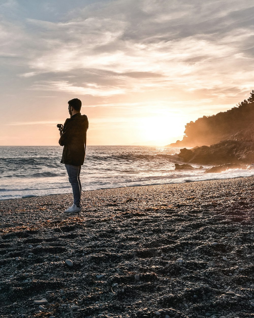Mann mit Jacke steht während der goldenen Stunde am Strand