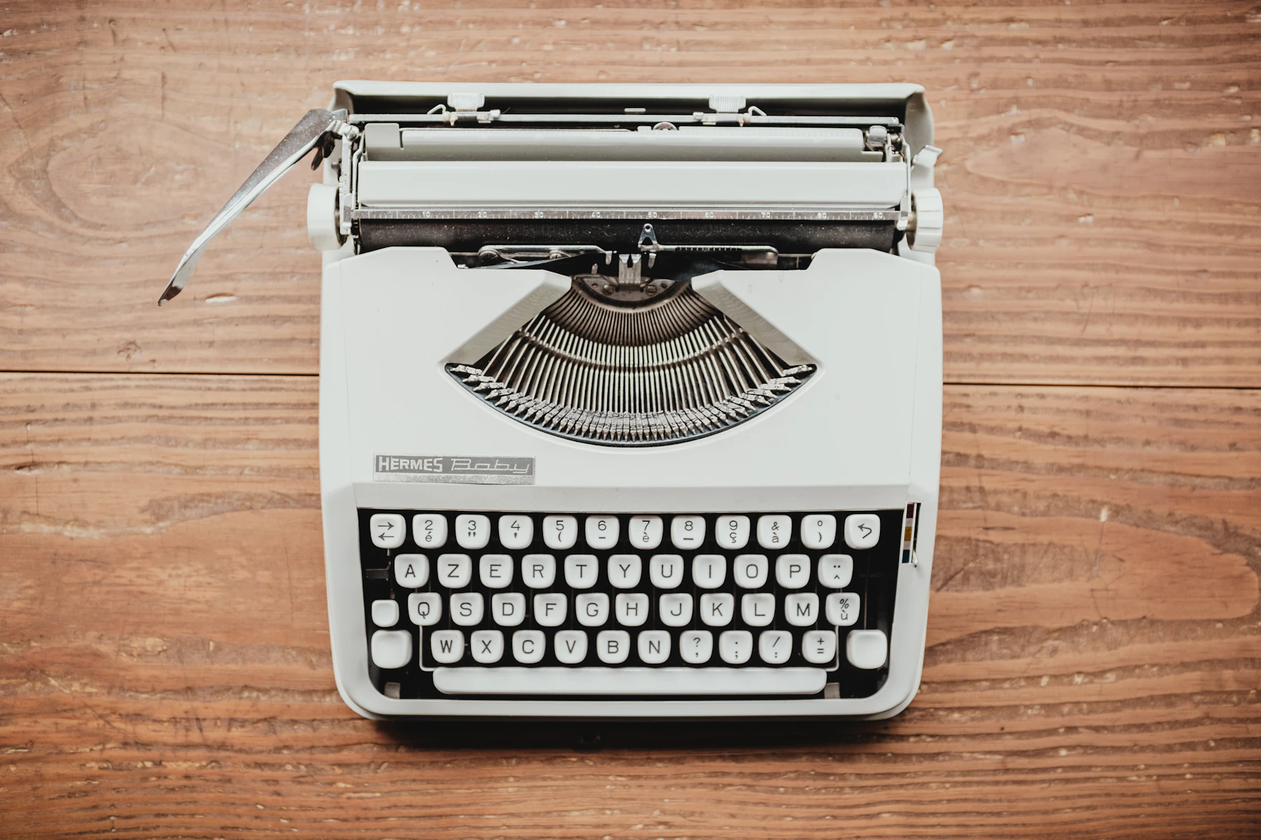A pale gray portable typewriter seen from above on a wooden table