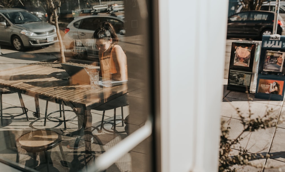 Mujer sentada junto a la ventana de vidrio usando computadora portátil