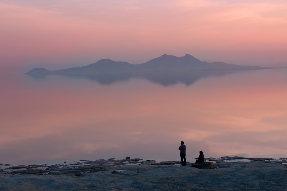 two person standing beside body of water