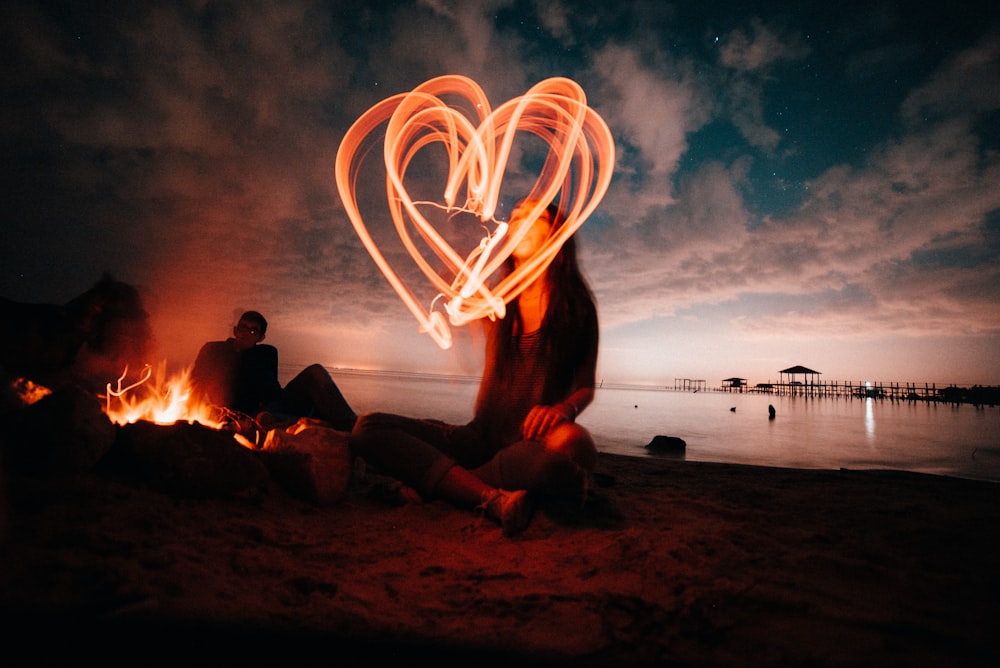 woman sitting on sand near bonfire