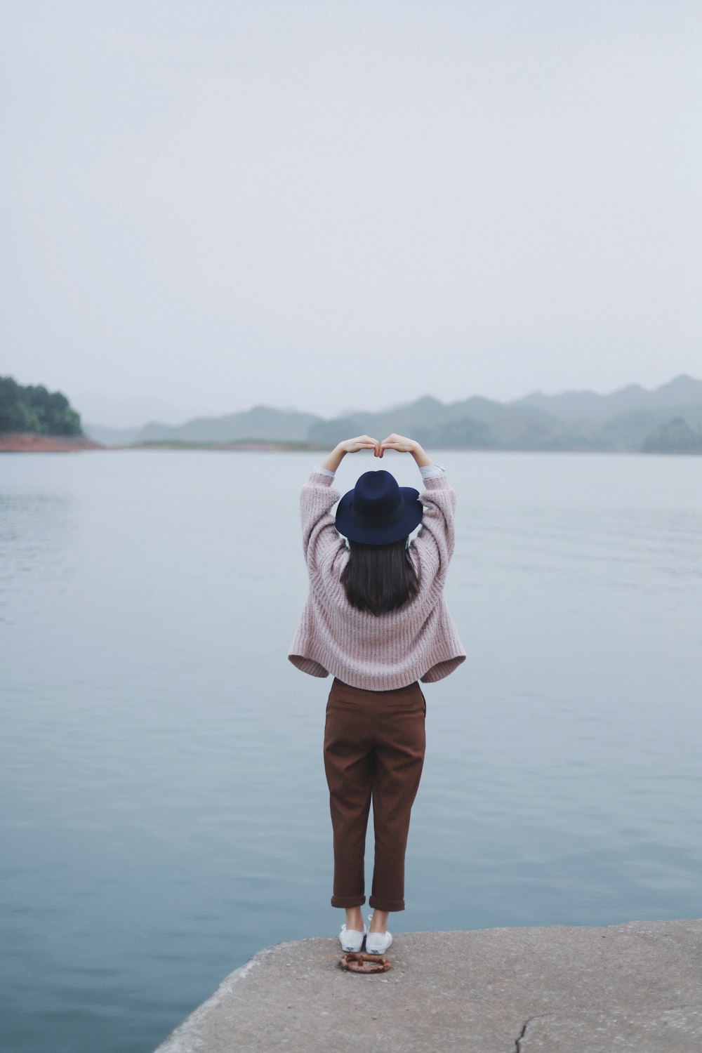 woman taking a heart pose beside body of water