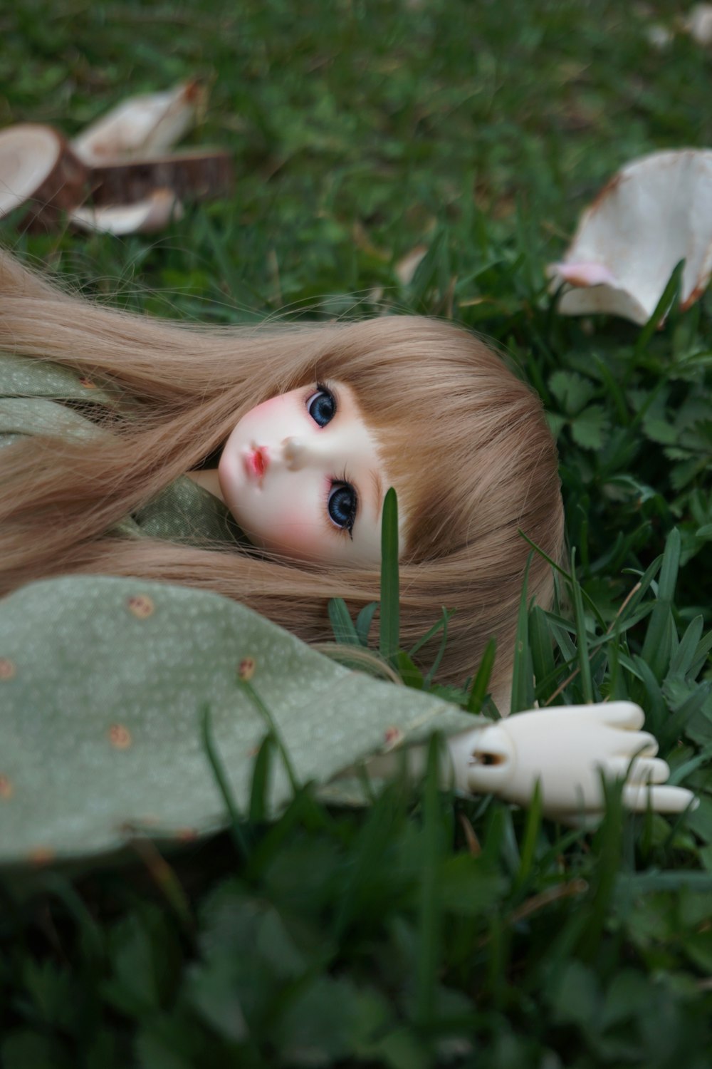 female doll in green dress laying on grass field