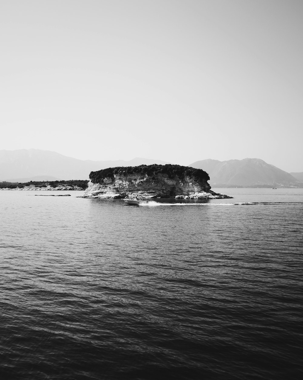 fotografia em tons de cinza do barco perto da ilha durante o dia
