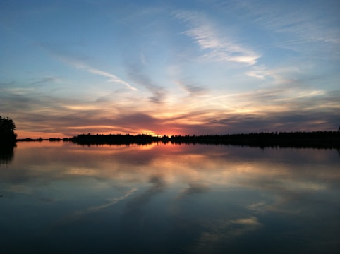Sunset over a quiet lake with reflections of colorful clouds.
