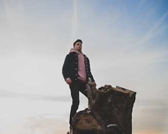 man in black jacket and pink pullover hoodie standing on tree log