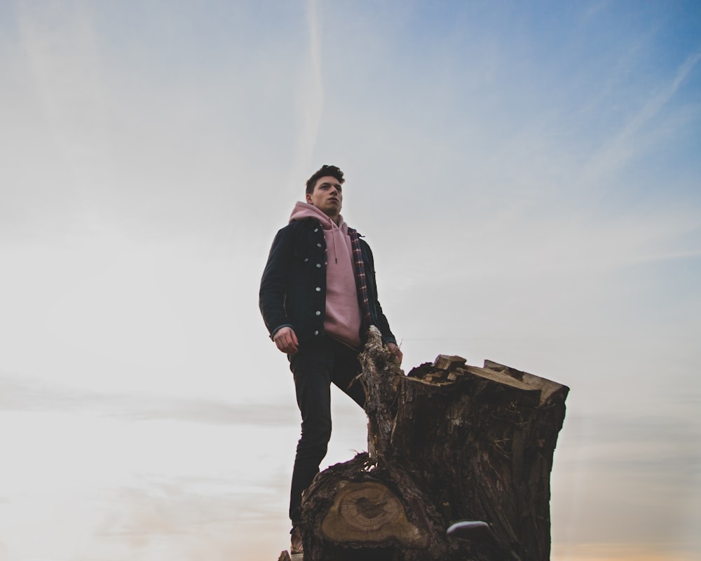 man in black jacket and pink pullover hoodie standing on tree log