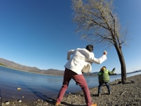 Kids laughing while skipping stones on a clear mountain lake at sunset.